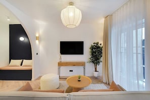 A modern living room with a flat-screen TV, a round wooden coffee table, a sofa, and a potted plant. - Chic Hideaway in Heart of Paris (Paris)