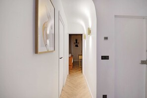 A hallway with a wooden floor, a white door, and a framed artwork on the wall. - Chic Hideaway in Heart of Paris (Paris)