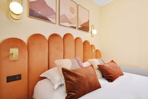 A hotel room with a unique curved headboard, a bed with white linens, and a wall-mounted light fixture. - Typical Parisian Flat next to the Louvre (Paris)