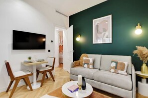 A modern living room with a sofa, a coffee table, a TV, and a dining area with chairs and a table. - Typical Parisian Flat next to the Louvre (Paris)