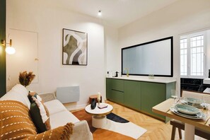 A modern living room with a sofa, a round coffee table, and a dining area with a table set for two. - Typical Parisian Flat next to the Louvre (Paris)