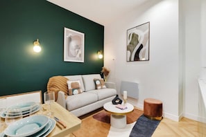 Een moderne woonkamer met een groene accentmuur, een bank met kussens, een salontafel en een eethoek met borden en bestek.