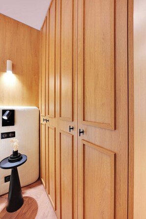 A wooden wardrobe with multiple doors, a small table with a vase, and a wall-mounted light fixture. - Elegant & Calm Flat close to Eiffel Tower (Paris)