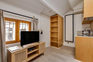 Ein kompakter Wohnraum mit Fernseher auf Holzständer, Schiebetürenschrank und einer Küchenzeile.