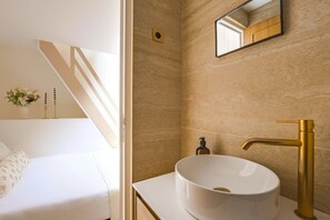 A modern bathroom with a white sink, gold faucet, and a mirror above it. - Live in a Hut in the Heart of Paris - Louvre (Paris)