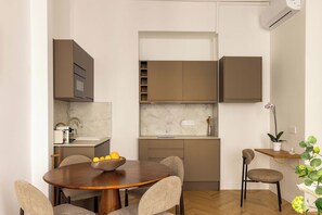 A modern kitchen with built-in appliances, a dining table with chairs, and a small side table with a plant. - Modern & Refined Flat in Prime Marais Location (Paris)