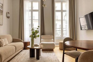 A living room with a sofa, armchair, coffee table, and a dining table. - Modern & Refined Flat in Prime Marais Location (Paris)