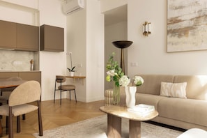 A modern living room with a sofa, a dining table with chairs, a coffee table with books, and a potted plant. - Modern & Refined Flat in Prime Marais Location (Paris)