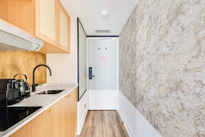 A narrow kitchen with wooden cabinets, a black kettle, and a marble backsplash. - Sweet Escape in Central Le Marais (Paris)