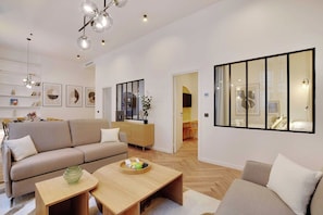 A modern living room with a sofa, coffee table, and decorative items. There is a dining area visible in the background. - Contemporary Flat by Champs Elysées & Parc Monceau (Paris)