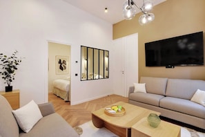 A modern living room with a sofa, a coffee table with fruit, a TV, and a plant. - Contemporary Flat by Champs Elysées & Parc Monceau (Paris)