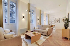 A modern living room with a sofa, a coffee table, and a dining area with chairs. - Contemporary Flat by Champs Elysées & Parc Monceau (Paris)
