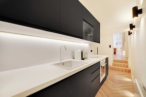 A modern kitchen with a white countertop, black cabinets, and a built-in microwave. - Contemporary Flat by Champs Elysées & Parc Monceau (Paris)