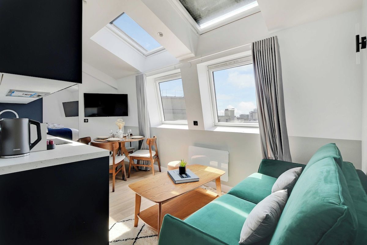 Un appartement moderne comprenant un coin repas, un canapé et une cuisine équipée d’une bouilloire.