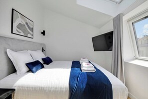 A hotel room with a bed, a flat-screen TV mounted on the wall, and a window with curtains. - Fabulous Getaway over the Parisian Clouds - 1BR (Paris)