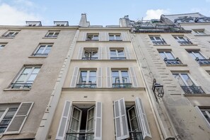 A multi-story building with white shutters, balconies, and a visible entrance. - Ideal Location in the Heart of Vibrant Le Marais (Paris)