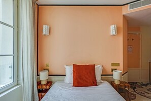 A hotel room with a bed, two bedside lamps, a window with curtains, and a wall-mounted air vent. - Ideal Location in the Heart of Vibrant Le Marais (Paris)
