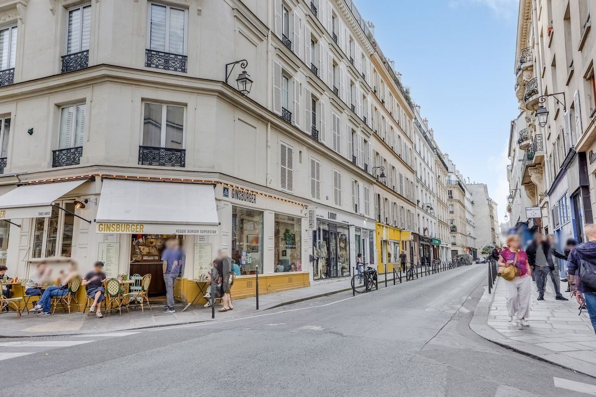 A street view with buildings, a restaurant named 'GINSBURGER,' and people sitting outside.