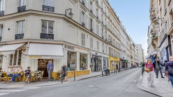 A street view with buildings, a restaurant named 'GINSBURGER,' and people sitting outside.