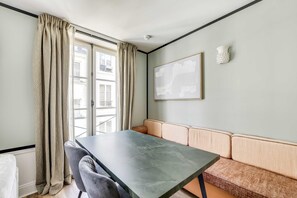 A room with a table, a bench, and a window with curtains. - Ideal Retreat in a Peaceful Marais Area (Paris)