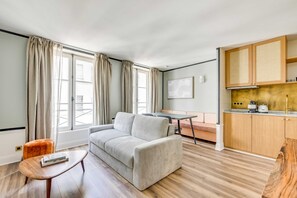 A modern living room with a sofa, a small table, and a kitchen area with wooden cabinets and a countertop. - Ideal Retreat in a Peaceful Marais Area (Paris)