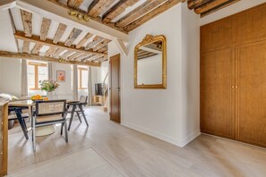 Ein Zimmer mit freiliegenden Holzbalken, einem Essbereich mit rundem Tisch und Stühlen, einem großen Spiegel und einem Kleiderschrank.