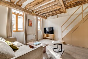 Ein modernes Wohnzimmer mit freiliegenden Holzbalken, einer Couch, einem Couchtisch, einem Fernseher und einer Treppe.