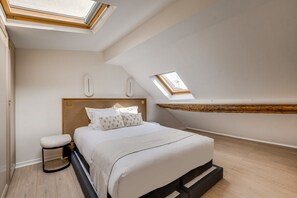 A bedroom with a bed, a nightstand, a skylight, and a wooden beam. - Splendid Duplex overlooking the Heart of Paris (Paris)