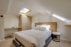 Ein Schlafzimmer mit Dachfenster, einem Bett mit Kopfteil, einem Nachttisch und einem kleinen Hocker.