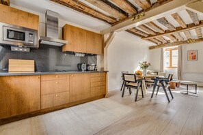 A modern kitchen with wooden cabinets, a built-in microwave, and a dining area with a table and chairs. - Splendid Duplex overlooking the Heart of Paris (Paris)