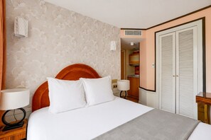 Une chambre d’hôtel avec un lit, une table de chevet, une lampe, une armoire et une salle de bain visible au fond.