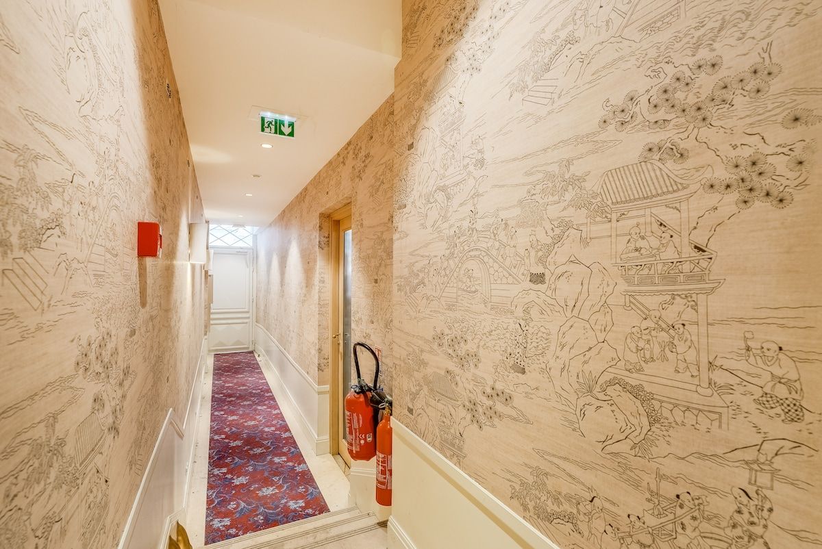 A hallway with patterned walls, a red carpet, and fire extinguishers.