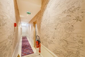 Un couloir aux murs ornés de motifs, un tapis rouge et des extincteurs.