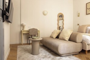 Ein Wohnzimmer mit einem beigen Sofa, einem runden Couchtisch, einem Sessel mit Leopardenmuster, einem kleinen Beistelltisch und einem wandmontierten Spiegel.