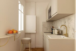 A compact kitchen with a marble countertop, a gold faucet, and a white cabinet. - Newly Renovated Flat in the Heart of Le Marais (Paris)