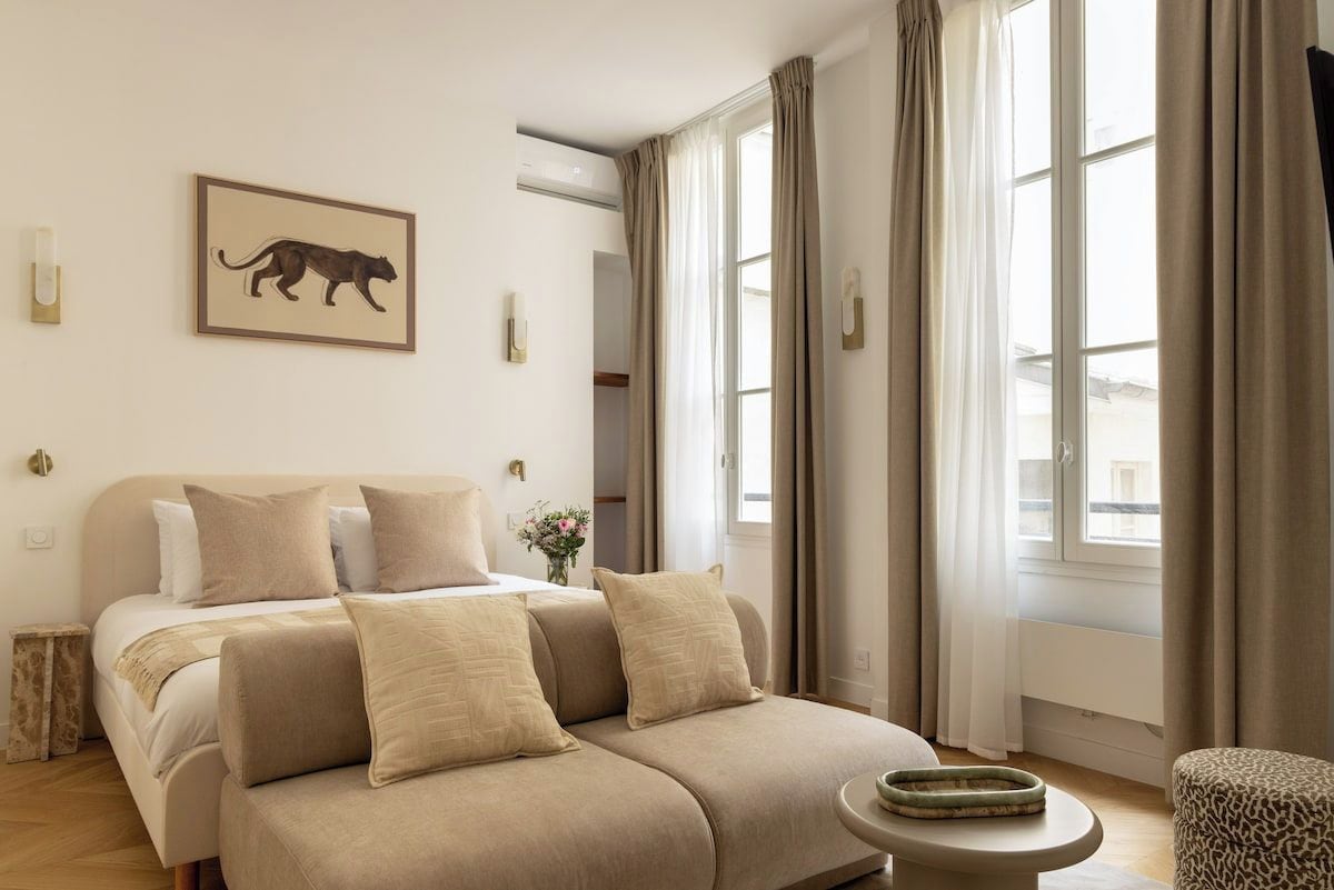 Ein Schlafzimmer mit Bett, Sofa, kleinem Tisch und einem Fenster mit Vorhängen.