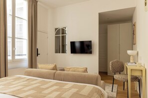 A hotel room with a bed, a television, a wardrobe, and a chair. - Newly Renovated Flat in the Heart of Le Marais (Paris)