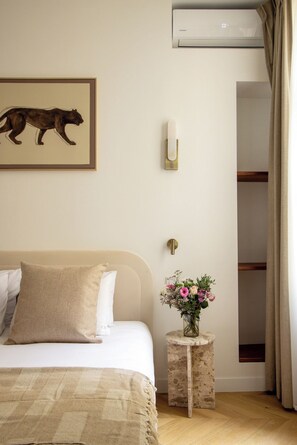 A bedroom with a bed, a wall-mounted air conditioner, a framed animal painting, a small side table with a vase of flowers, and a closet. - Newly Renovated Flat in the Heart of Le Marais (Paris)