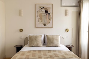 Ein Hotelzimmer mit einem Bett, zwei Nachttischen, einer Wand-Klimaanlage und einem gerahmten abstrakten Kunstwerk.