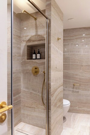 Ein modernes Badezimmer mit einer gläsernen Dusche, Marmorwänden und einer Toilette.