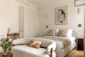 Ein Schlafzimmer mit einem Bett, einem Schlafsofa, einem Nachttisch, einer Vase mit Blumen und einem Bild an der Wand.