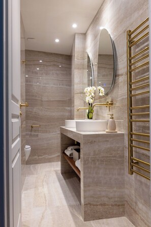 A modern bathroom with a marble vanity, a gold-framed mirror, and a towel rack. - New Central Stylish Flat in Le Marais (Paris)