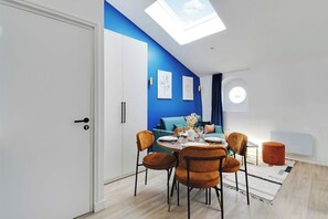 A modern living room with a dining area, a blue accent wall, a skylight, and a round table with chairs. - Dream Stay in the Parisian Sky - Voltaire/Nation (Paris)
