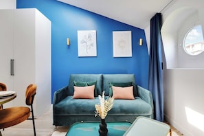 Ein modernes Wohnzimmer mit blauer Akzentwand, einem grünen Sofa mit rosafarbenen Kissen, einem runden Couchtisch und einer Vase mit getrockneten Blumen.