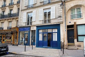 A street view with a building featuring a blue storefront, a visible number '12' on the facade, and a parked car. - Live Like Emily in Paris in Her Neighbourhood ! (Paris)