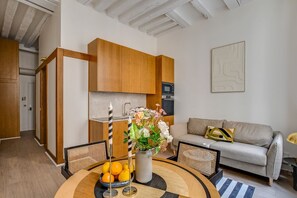 A modern kitchen with wooden cabinets, a dining area with a round table, and a sofa. - Location, location, location - 1BR near Louvre (Paris)