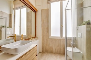 A modern bathroom with a large mirror, two sinks, a shower enclosure, and a window. - Location, location, location - 1BR near Louvre (Paris)