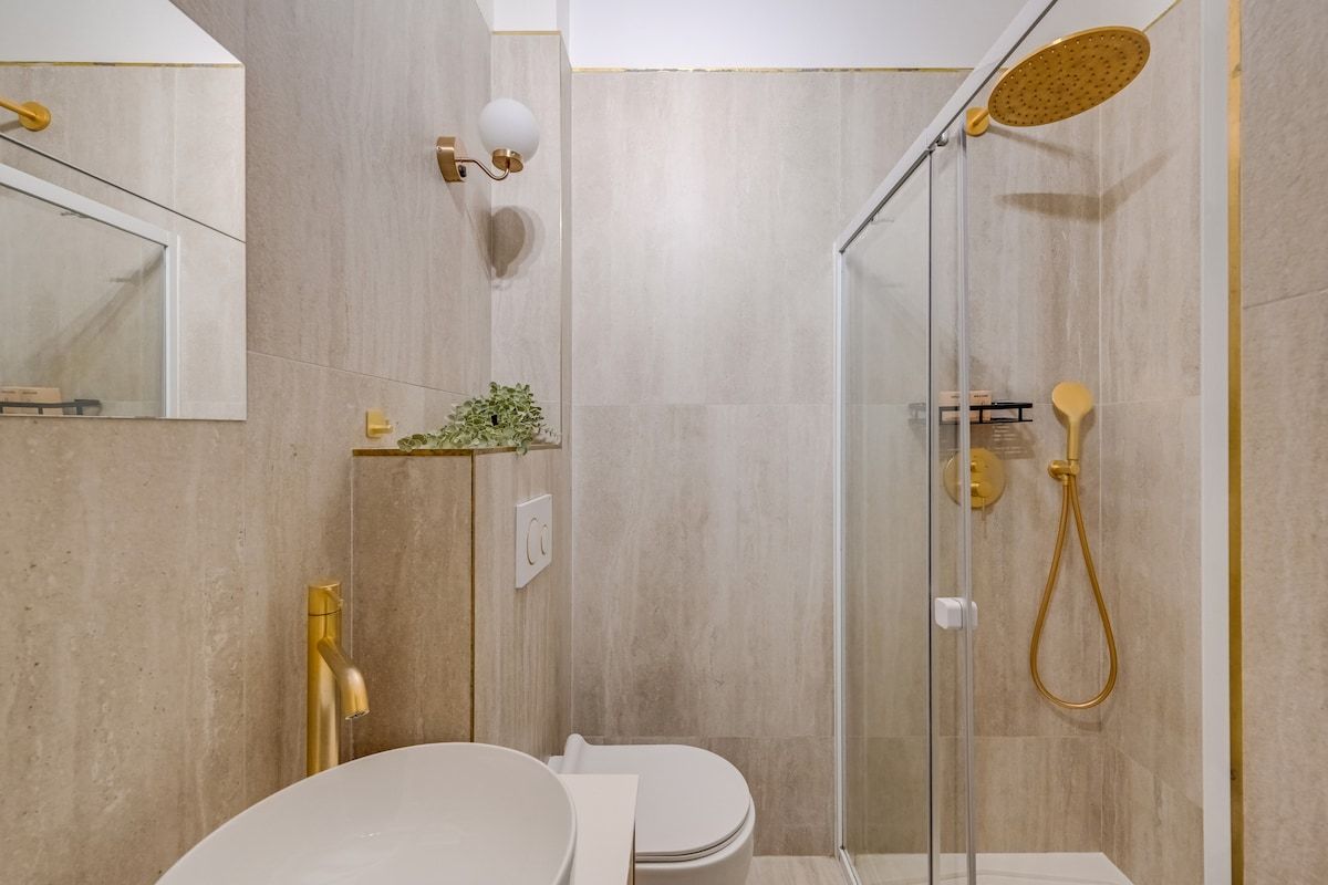 Une salle de bain moderne avec une douche à parois de verre, des toilettes blanches et un robinet doré.