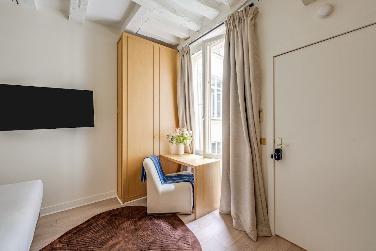 Une pièce comprenant un lit, un bureau, une chaise, une fenêtre avec des rideaux et une porte.