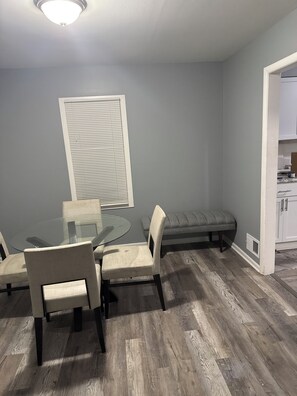 A dining area with a glass table, chairs, a bench, and a window with blinds. - Cozy 2-bedroom house in peaceful Harvey with AC (Harvey)